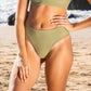 Waist down pic of a woman in a sage green bikini at the beach