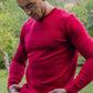 Lifestyle image of a man pulling down the hem of the red crew neck sweater