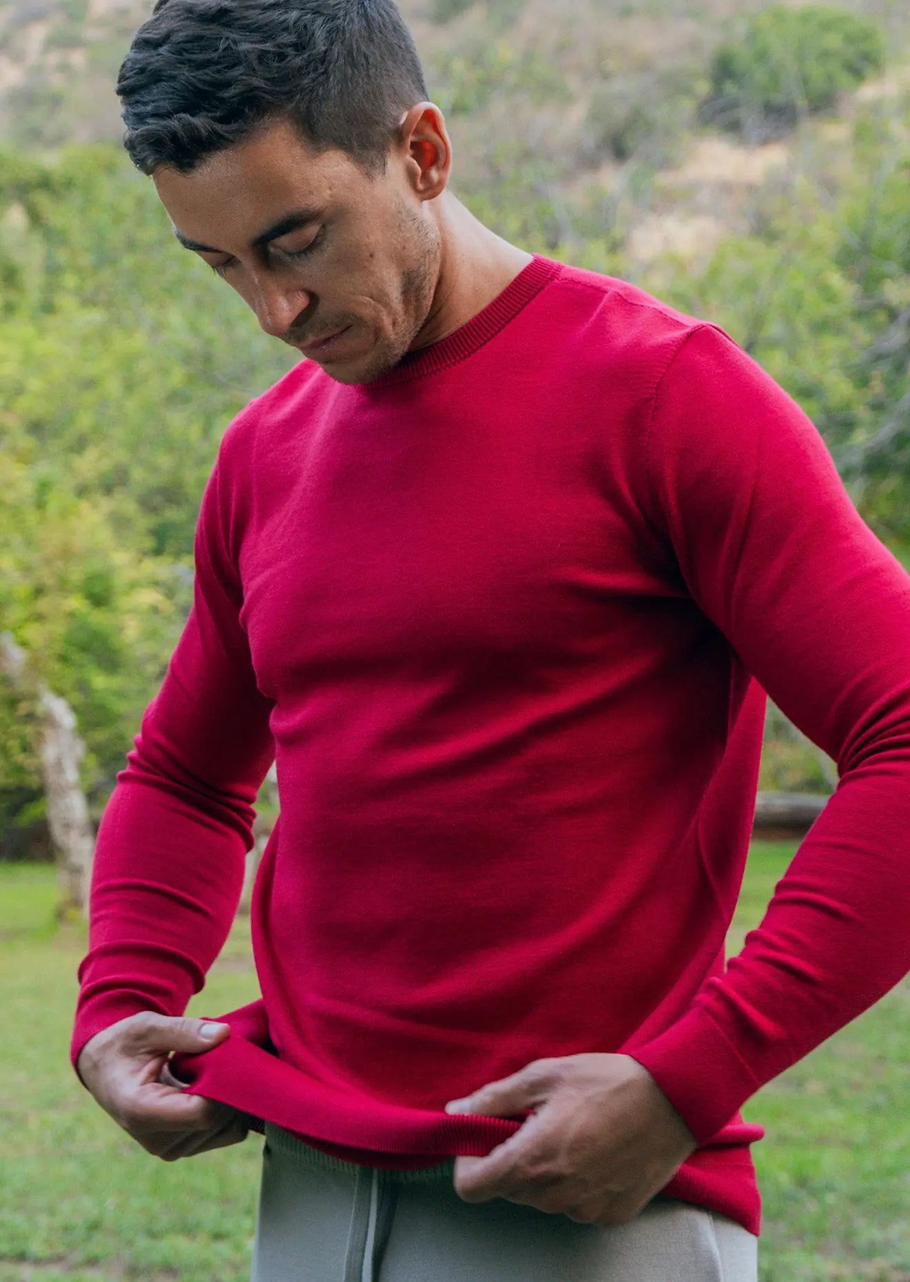 Lifestyle image of a man pulling down the hem of the red crew neck sweater