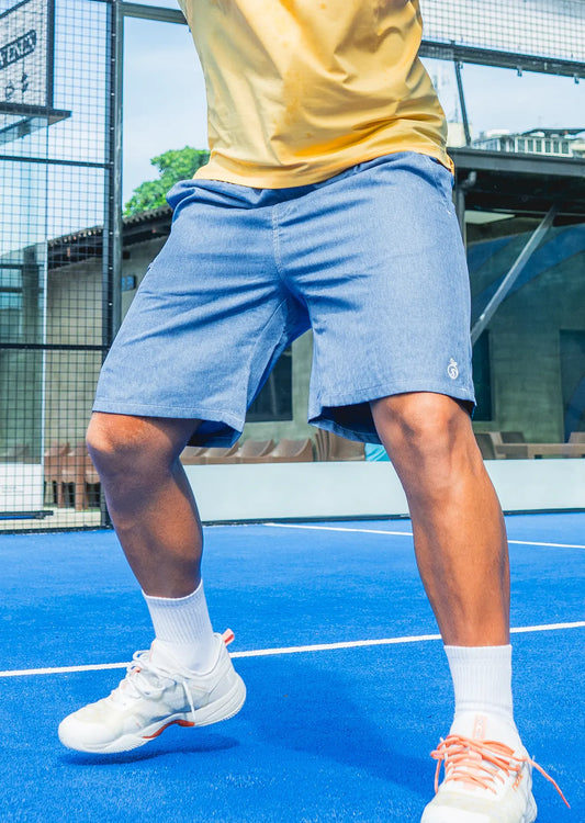 Men's blue Haven Swim Trunks paired with a yellow polo on a tennis court for a sporty look