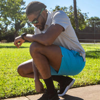 Model kneeling while wearing the Men's Retro 5" Inseam Swim Trunks in blue and a gray polo shirt