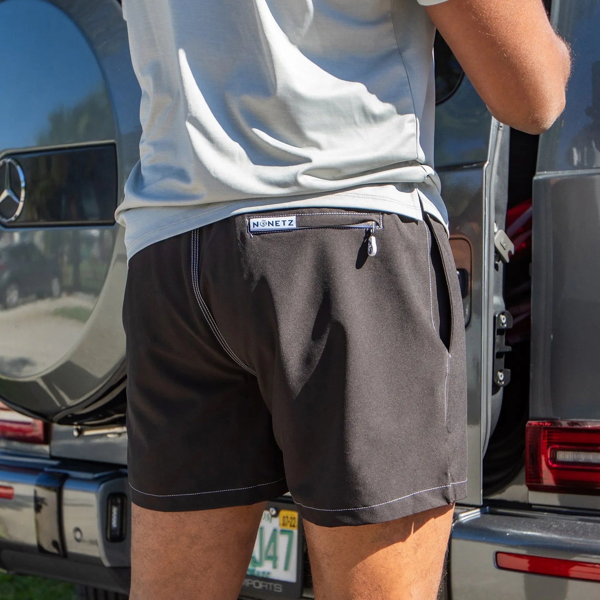 A man modeling the Men's Retro 5" Inseam Slim Fit Swim Trunks beside a vehicle